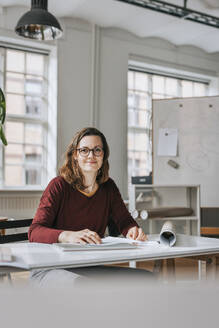 Porträt einer lächelnden Geschäftsfrau, die am Schreibtisch im Büro sitzt - MASF36824