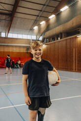 Smiling boy with disability holding soccer ball while standing at sports court - MASF36862