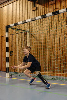 Boy with disability goalkeeping near net while playing football at sports court - MASF36865