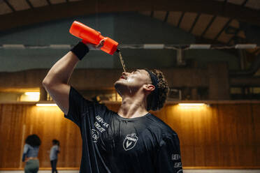 Männlicher Sportler, der sich auf dem Sportplatz Wasser aus einer Flasche ins Gesicht gießt - MASF36875