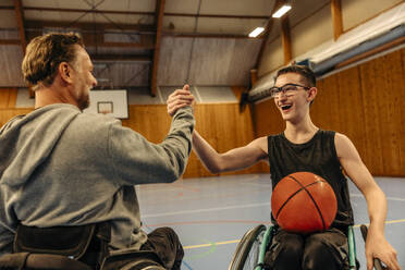 Cheerful male and female athletes with disabilities doing handshake while playing basketball at sports court - MASF36895