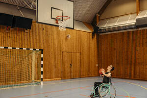 Mädchen spielt Basketball im Rollstuhl sitzend auf einem Sportplatz - MASF36896