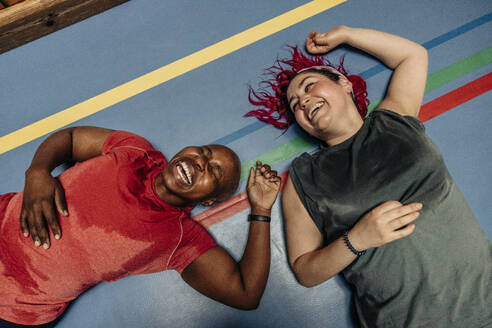 High angle view of female athletes laughing while lying on safety mat at sports court - MASF36903