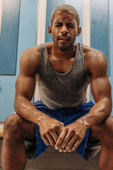 Tired male athlete with eyes closed sitting on bench in locker room - MASF36904