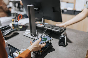 Cropped image of customer scanning credit card reader while paying through smart phone in electronics store - MASF36926