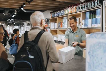 Smiling sales clerk scanning appliance box while customers at checkout counter in electronics store - MASF36932