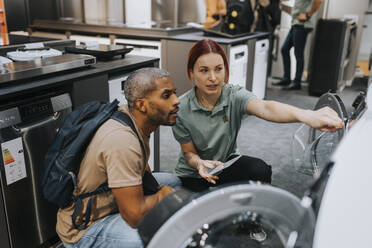 Saleswoman advising male customer in buying washing machine at appliances store - MASF36945