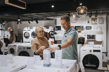 Salesman advising senior woman in buying appliance at electronics store - MASF36947