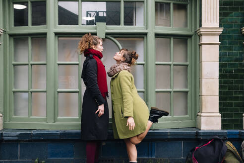 Junge Frau auf einem Bein stehend mit Freundin vor einem Fenster - AMWF01366