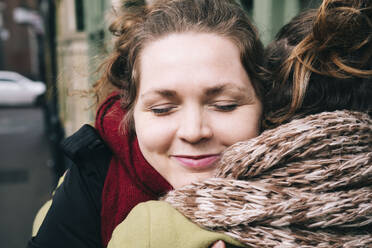 Lächelnde Frau mit geschlossenen Augen, die eine Freundin umarmt - AMWF01367