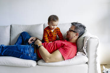 Father lying on sofa with son at home - JJF00960