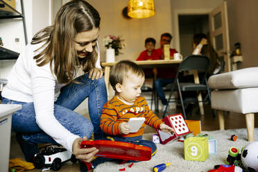 Mutter hockt bei ihrem Sohn, der zu Hause mit Spielzeug spielt - JJF00962