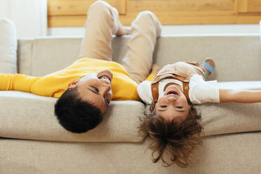 Playful woman lying down on sofa with son at home - EBSF03288