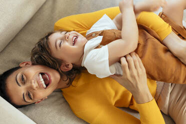 Cheerful woman tickling son on sofa at home - EBSF03289