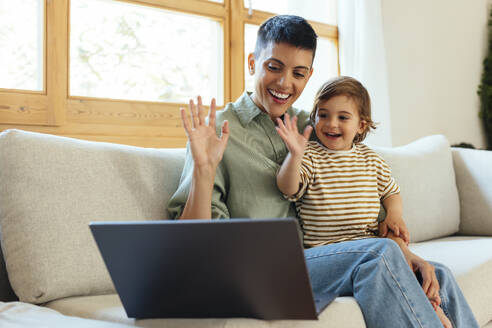 Happy mother with son waving on video call through laptop at home - EBSF03295