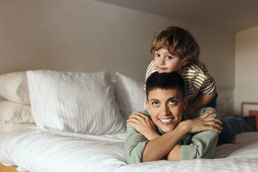 Smiling woman lying with son on bed at home - EBSF03296