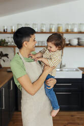 Smiling woman wearing apron and playing with son at home - EBSF03297