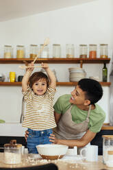 Glückliche Frau mit Sohn, der in der Küche zu Hause eine Kelle hält - EBSF03304