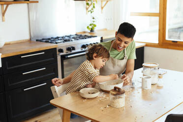 Mother and son preparing food at dining table in kitchen - EBSF03305