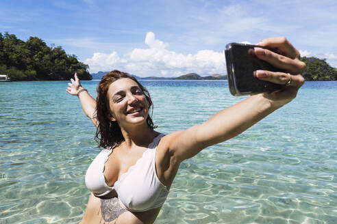 Carefree woman taking selfie through smart phone in sea at vacation - PNAF05272