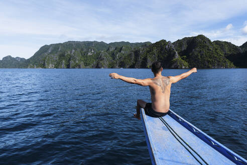 Man with arms outstretched sitting on ship's bow at vacation - PNAF05275