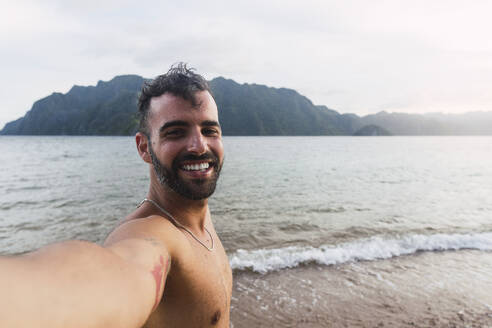 Glücklicher Mann ohne Hemd nimmt Selfie am Ufer - PNAF05280