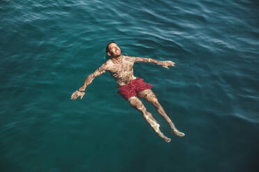 Carefree young man swimming in sea at vacation - PCLF00499