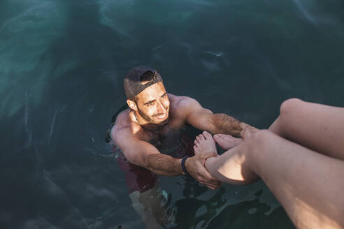Lächelnder Mann im Meer, der im Urlaub an den Beinen eines Teenagermädchens zieht - PCLF00505