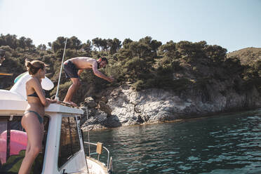 Mann taucht im Urlaub auf einer Yacht stehend ins Wasser - PCLF00508