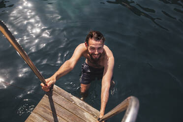 Lächelnder Mann ohne Hemd, der sich nach dem Schwimmen im Meer auf den Stufen bewegt - PCLF00509