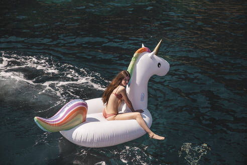 Girl sitting on unicorn air mattress in sea at vacation - PCLF00529