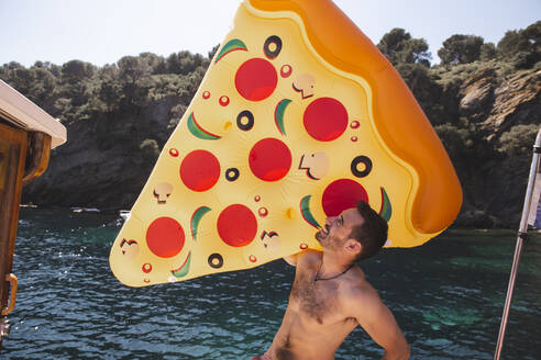 Mann ohne Hemd hält pizzaförmige Luftmatratze im Urlaub - PCLF00533