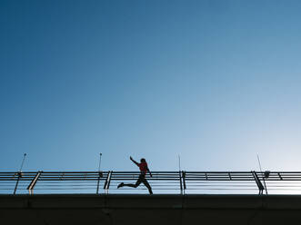 Sportler läuft in der Nähe des Geländers unter klarem blauen Himmel - EGAF02592