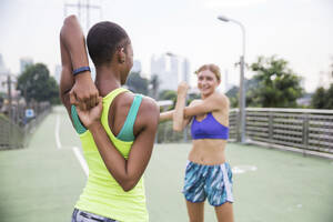 Woman in sports clothing stretching with friend on footpath - IKF00463