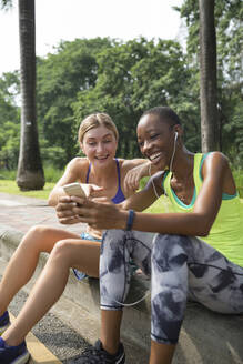 Glückliche Freunde teilen sich ein Smartphone im Park - IKF00487