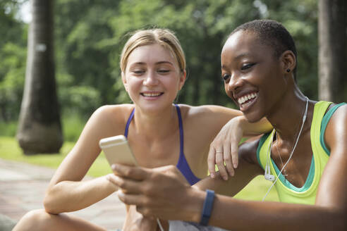 Lächelnde gemischtrassige Freunde teilen sich ein Handy im Park - IKF00488