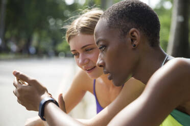 Seriöse Frauen teilen sich ein Smartphone im Park - IKF00490