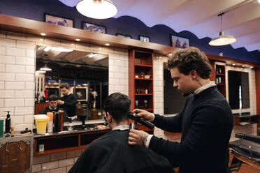 Barber cutting hair of customer with electric razor in shop - ACPF01553
