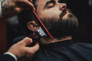 Customer with eyes closed getting beard trimmed in barber shop - ACPF01554