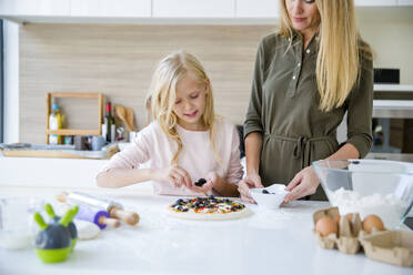 Girl preparing pizza with mother in kitchen at home - IKF00495