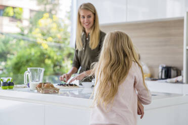 Blond girl with mother preparing pizza in kitchen at home - IKF00497
