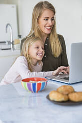 Lächelnde Tochter lernt mit ihrer Mutter zu Hause den Umgang mit dem Laptop - IKF00503