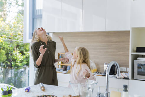 Playful daughter enjoying with mother in kitchen at home - IKF00511