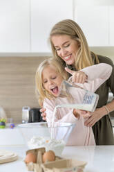 Lächelnde Frau, die ihrer Tochter hilft, zu Hause Milch in Mehl zu gießen - IKF00517