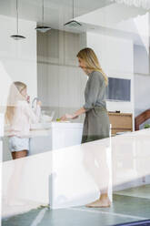 Mother and daughter preparing food seen through glass window - IKF00518