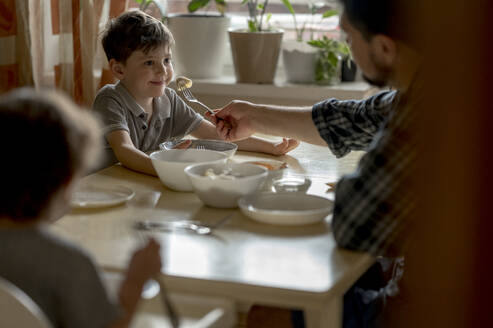 Vater füttert Sohn am Esstisch zu Hause mit Knödel - ANAF01395
