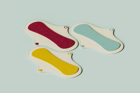 3D render of yellow, red and green sanitary pad flat laid against green background - GCAF00326