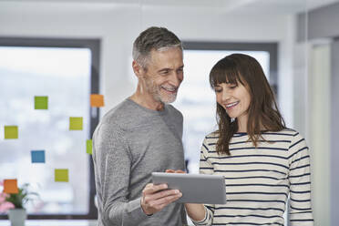 Businessman showing over tablet PC to smiling colleague in office - RORF03513