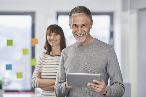 Smiling senior businessman holding tablet PC with colleague at workplace - RORF03525