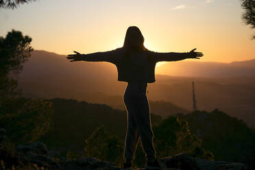 Silhouette einer Frau mit ausgestreckten Armen bei Sonnenuntergang - DMHF00001